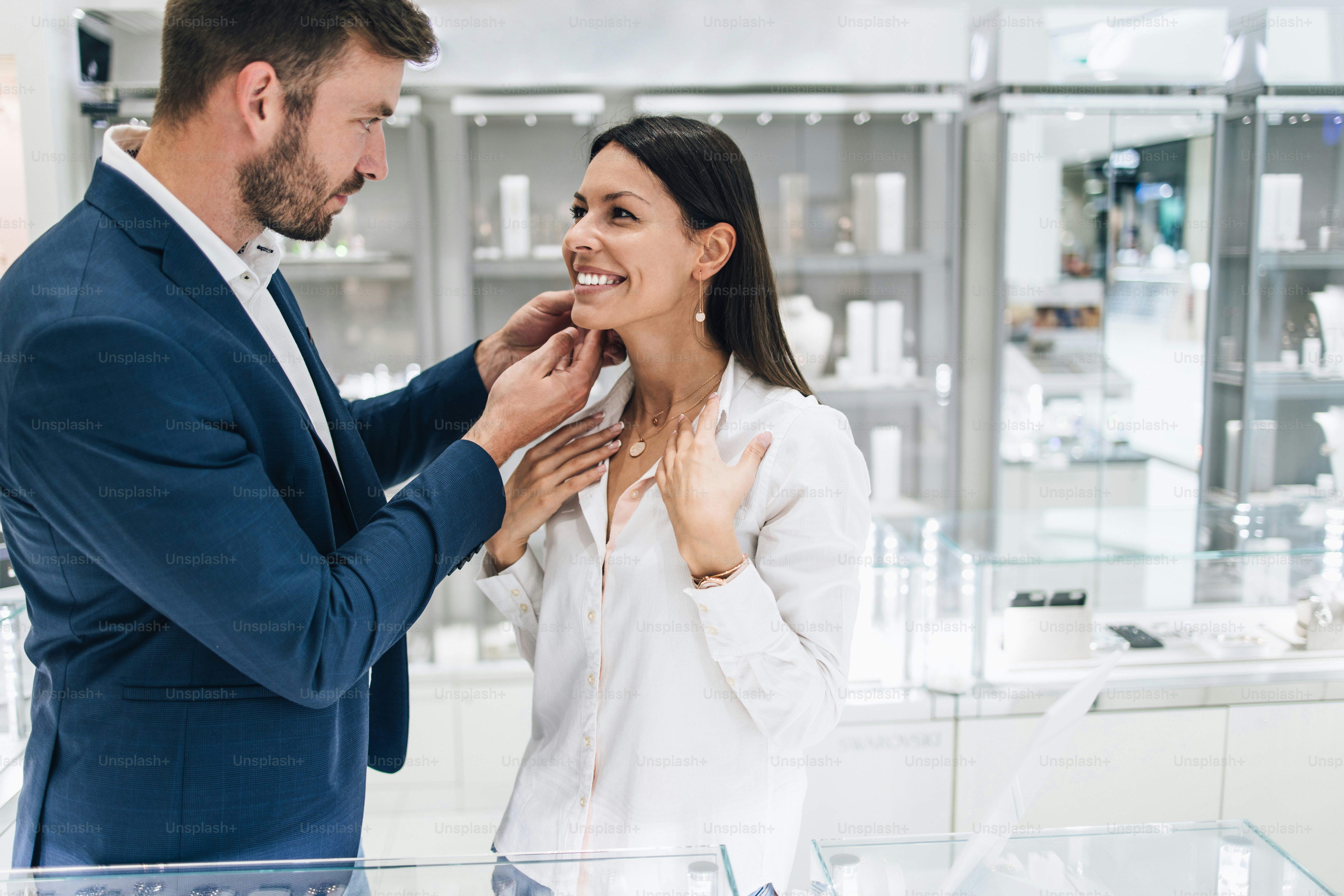 Beautiful couple enjoying in shopping at modern jewelry store. Young woman try it out gorgeous necklace and earrings.